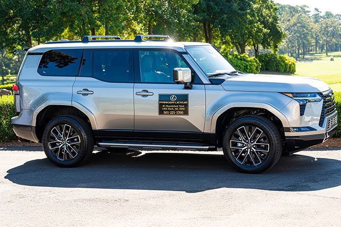Golfing for a Good Cause; Silver SUV with a dealership sign parked on a sunny street. The shiny vehicle contrasts with the lush green trees and grass in the background.