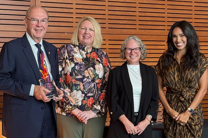 Harry Robinson Receives BBB Torch Award; Four people stand smiling in front of a wooden panel wall. One person holds a colorful glass award. They convey a sense of achievement and happiness.