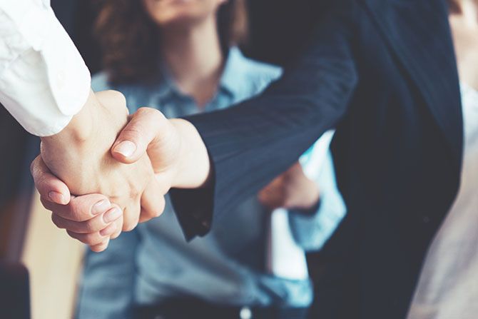 President’s Message: The Power of Partnerships; Close-up of two people shaking hands, one in a dark suit and the other in a white shirt. A third person stands in the background, fostering a professional tone.